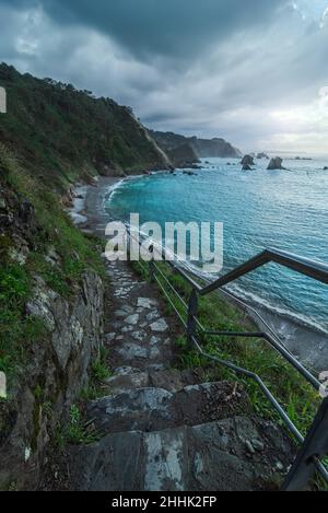 Lange Treppe mit Geländer am Strand von Playa del Silencio mit Berg mit grünen Pflanzen in der Nähe plätscherndes Meer in der Natur bedeckt Stockfoto