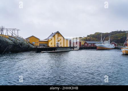 Malerische Aussicht auf kleine Siedlung mit typischen bunten Wohnhäusern am Meer umgeben von riesigen felsigen Bergen unter nebligen Himmel in Nusfjord vil Stockfoto