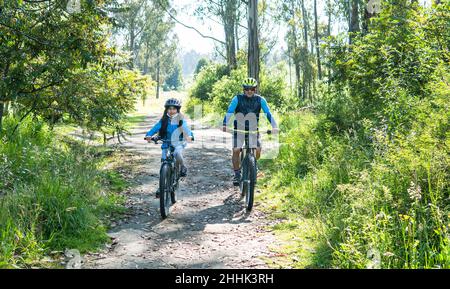 Ein Vater und eine Tochter fahren mit dem Mountainbike auf einer Landstraße im Wald Stockfoto