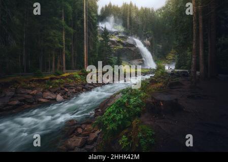 Lange Exposition der Krimmler Kaskade fällt von felsigen Klippen zwischen Wäldern mit hohen grünen Nadelbäumen in der Natur von Österreich am Sommertag Stockfoto