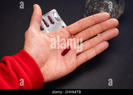 Person, die Medikamente mit schwarzem Hintergrund mit Blister und Wasser nimmt. Stockfoto