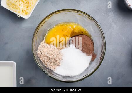 Draufsicht auf Glasschüssel mit Zutaten für süße Schokoladenwaffeln mit Rohrzucker und Kakao auf grauem Hintergrund in der Küche Stockfoto