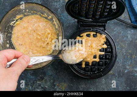 Von oben von Ernte anonyme Person Gießen süßen Käse Waffelteig auf Metall Waffeleisen beim Kochen am Tisch in der Küche Stockfoto
