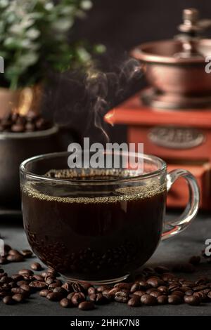 Ein Glas frisch gebrühten aromatischen Kaffees auf einer Untertasse, die mit verstreuten Bohnen gegen das manuelle Mahlwerk gelegt wird Stockfoto