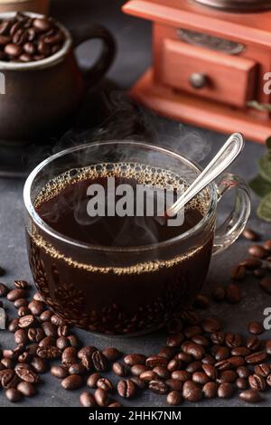 Ein Glas frisch gebrühten aromatischen Kaffees auf einer Untertasse, die mit verstreuten Bohnen gegen das manuelle Mahlwerk gelegt wird Stockfoto