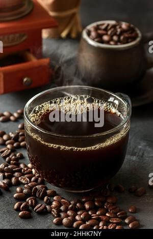 Ein Glas frisch gebrühten aromatischen Kaffees auf einer Untertasse, die mit verstreuten Bohnen gegen das manuelle Mahlwerk gelegt wird Stockfoto