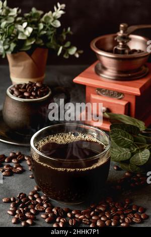 Ein Glas frisch gebrühten aromatischen Kaffees auf einer Untertasse, die mit verstreuten Bohnen gegen das manuelle Mahlwerk gelegt wird Stockfoto