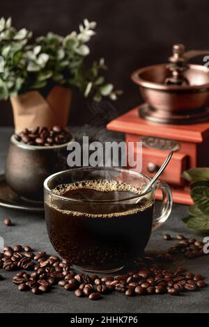 Ein Glas frisch gebrühten aromatischen Kaffees auf einer Untertasse, die mit verstreuten Bohnen gegen das manuelle Mahlwerk gelegt wird Stockfoto