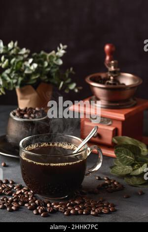 Ein Glas frisch gebrühten aromatischen Kaffees auf einer Untertasse, die mit verstreuten Bohnen gegen das manuelle Mahlwerk gelegt wird Stockfoto