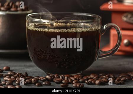 Ein Glas frisch gebrühten aromatischen Kaffees auf einer Untertasse, die mit verstreuten Bohnen gegen das manuelle Mahlwerk gelegt wird Stockfoto