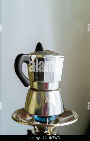 Moderne Mokakapfanne aus Metall zum Brühen von Kaffee auf einem Edelstahl-Gasherd in einer hellen Küche mit Tassen auf verschwommenem Hintergrund Stockfoto