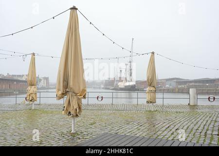 Lübeck, 21. Januar 2022: Gefaltete Schirme in einem Straßencafé direkt am Hafenquay der Trave an einem regnerischen nebligen Tag ohne Touri Stockfoto