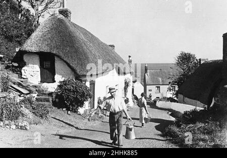 Ein Mann schleppt eine Abwanderung von Milch auf die Hauptfarafare in Clovelly. Das Dorf liegt in einem steilen Hang und hat nur eine einzige gepflasterte Hauptstraße, die sich den Hang hinunter schlängelt durch traditionelle weiß getünchte Hütten, die mit Fuchsien und Geranien bewaldet sind. Circa August 1935 Stockfoto