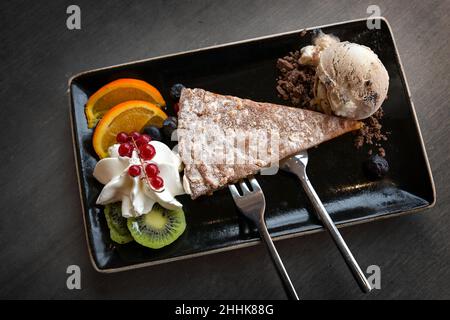 Mandelkuchen mit Eis und Früchten auf einem schwarzen Teller und einem dunkelgrauen Tisch, leckeres Dessert, Blick von oben Stockfoto
