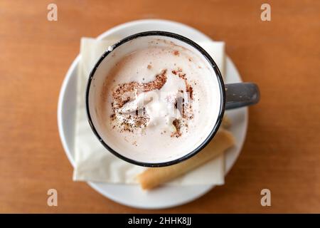 Heißer Schokoladendrink mit Schlagsahne und Kakaopulver, serviert mit einem Cookie in einem Becher auf einem Holztisch, Kopierraum, Blick von oben, selec Stockfoto
