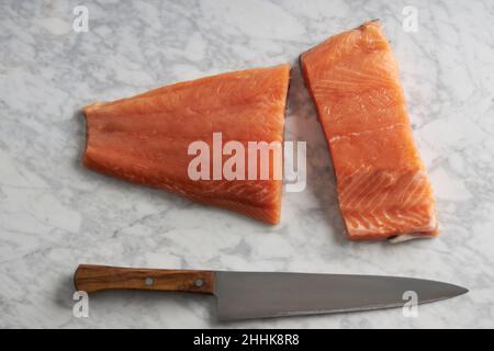 Draufsicht auf rohes Lachsfilet, das auf einer Marmorplatte auf einem Holztisch platziert ist Stockfoto