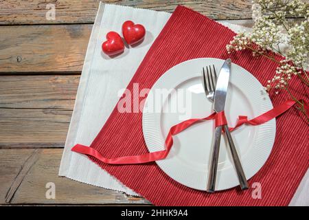 Tischkulisse für ein romantisches Dinner mit zwei Herzen, Pastete und Besteck auf rot-weißen Servietten, Liebeskonzept, rustikaler Holztisch mit Kopierfläche, Hig Stockfoto