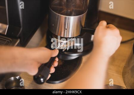 Hoher Winkel der Ernte anonyme Barista Zubereitung von frisch gemahlenem Kaffee in portafilter der professionellen Mühle im Café Stockfoto