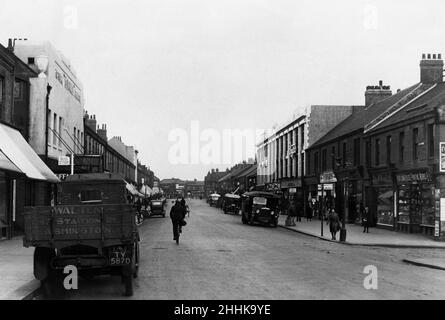 Ashington ist eine Stadt und eine zivile Gemeinde in Northumberland England. Mit einer Bevölkerung von rund 27.000, gemessen bei 27.764 bei der Zählung 2011, war es einst ein Zentrum des Kohlebergbaus. Die Stadt liegt etwa 15 Meilen (24 km) nördlich von Newcastle upon Tyne und westlich der A189. Der Süden der Stadt grenzt an den Fluss Wansbeck. Die Nordseeküste bei Newbiggin-by-the-Sea ist etwa 3 Meilen (5 km) vom Stadtzentrum entfernt.(Abbildung zeigt) Ashington's Station Road. 29th Mai 1932 Stockfoto