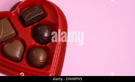 Herzförmige Schachtel mit Schokoladenbonbons auf einem rosa Hintergrund mit Platz für die Nachricht zum Valentinstag. Stockfoto