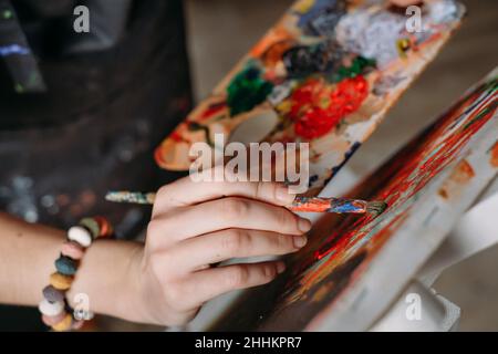 Hand mit Pinsel des Malers arbeiten in echten Studio mit Ölfarben, Schaffung von Leinwand, moderne Kunst. Junge Frau Künstlerin, Nahaufnahme Draufsicht auf Palette Stockfoto