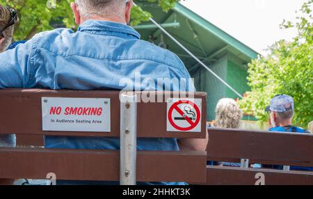 Ein RAUCHVERBOTSSCHILD auf der Rückseite einer Holzbank in einem Konzertsaal im Freien. Stockfoto