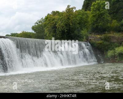 An einem bewölkten Tag steigt Nebel aus einem Weir Wasserfall am Root River in Lanesboro, Minnesota. Stockfoto