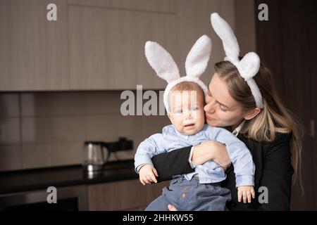 Glückliche Familie Mutter und Baby mit Hasenohren, fürsorgliche Mutter mit kleinen Sohn in den Armen, Vorbereitung auf Ostern Urlaub, glückliche Mutterschaft und Kindheit Stockfoto