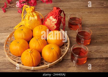 Chinesische Neujahrsgeschenke mit Glückstickereien in Teller mit Mandarinen und Tassen Tee auf dem Tisch Stockfoto