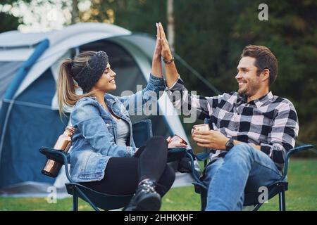Junges nettes Paar, das auf Stühlen vor dem Zelt auf dem Camping sitzt Stockfoto