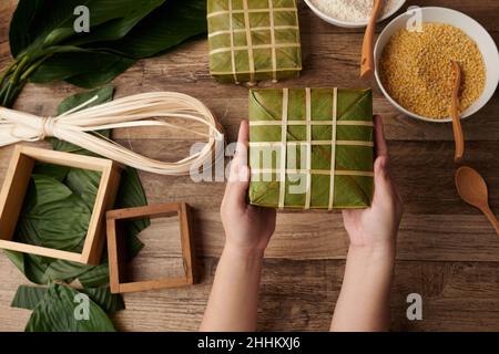 Hände einer Frau, die gewickelten klebrigen Reiskuchen hält, machen sie FOC Chinesisches Neujahr Stockfoto