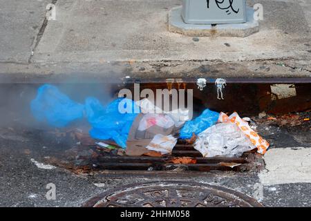 Ein dampfender Müllhaufen, der einen Sturmabfluss, ein Auffangbecken und ein Kanalrost in New York, NY, verstopft. Stockfoto