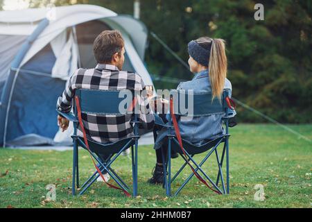 Junges nettes Paar, das auf Stühlen vor dem Zelt auf dem Camping sitzt Stockfoto