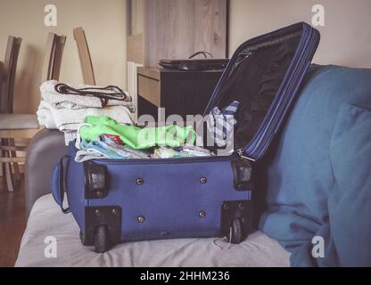 Nahaufnahme eines blauen Koffers voller Kleidung, die vor einer Reise auf dem Sofa liegt Stockfoto