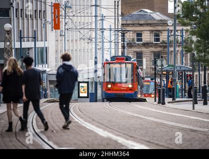 Sheffield, Großbritannien Supertram fährt durch das Einkaufsviertel im Stadtzentrum, mit Fußgängern und Einkäufern auf der Straße, während die Straßenbahn auf der High Street fährt Stockfoto