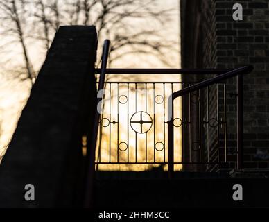 Sonnenuntergang hinter dem Kirchentor mit Kreuzkreuzzeichen in Metallgeländern. Wunderschöner orange-goldener Sonnenuntergang. Stockfoto