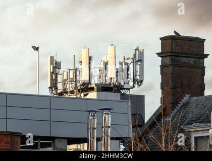 5G Mobilfunk-Funkmastsender bei Sonnenuntergang in Wohnstadt mit alten 4G und 3G Antennen ebenfalls angeschlossen. Gebäude unter hellem Himmel Stockfoto