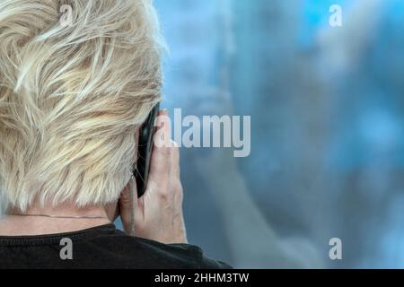 Eine Frau, die auf dem Handy spricht und gegenüber dem Fenster steht, wurde in einem Innenfoto abgeschnitten Stockfoto