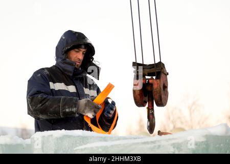 Der Schleuder zieht eine Bandschlinge am Haken eines LKW-Krans an Stockfoto