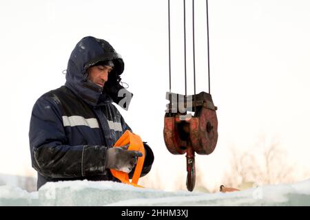 Der Schleuder zieht eine Bandschlinge am Haken eines LKW-Krans an Stockfoto