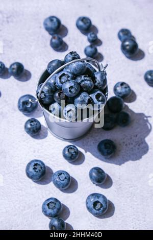 Heidelbeeren in einem kleinen Eimer auf Betongrund. Gesunde Bio saisonalen Obst Hintergrund. Bio-Lebensmittel. Gesunder Sommersnack. Speicherplatz kopieren Stockfoto