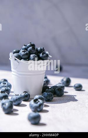 Heidelbeeren in einem kleinen Eimer auf Betongrund. Gesunde Bio saisonalen Obst Hintergrund. Bio-Lebensmittel. Gesunder Sommersnack. Speicherplatz kopieren Stockfoto