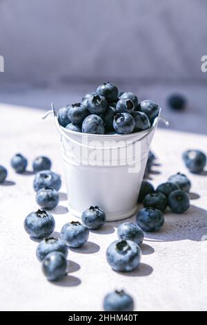 Heidelbeeren in einem kleinen Eimer auf Betongrund. Gesunde Bio saisonalen Obst Hintergrund. Bio-Lebensmittel. Gesunder Sommersnack. Speicherplatz kopieren Stockfoto