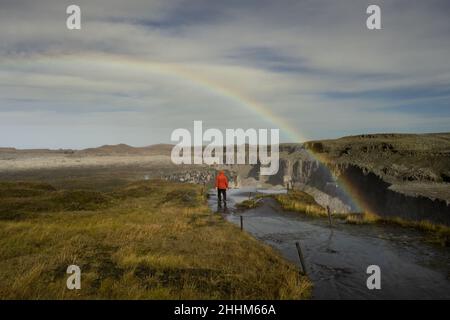 Ein Mann in einer roten Jacke steht unter dem Regenbogen Stockfoto