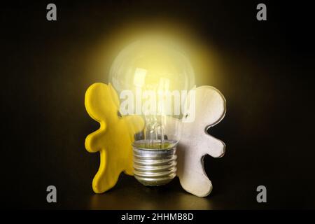 Zwei Männer aus Plastilin halten eine beleuchtete Glühbirne auf schwarzem Hintergrund. Teamwork-Konzept. Kreative neue Idee. Innovation, Brainstorming, Inspiration und sol Stockfoto