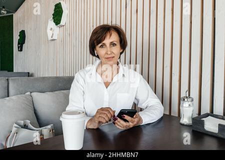 Leitende Geschäftsfrau arbeitet im Café. Remote-Arbeit mit dem Mobiltelefon. Stockfoto