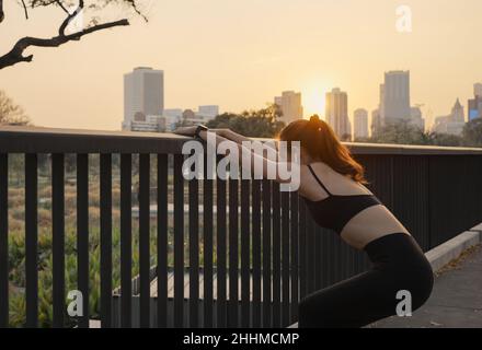 Junge Frau in Sportkleidung, die bei Sonnenuntergang auf der Brücke in der Stadt unterwegs ist. Stockfoto