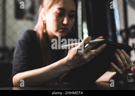 Portrait einer professionellen Tätowiererin in einem Tattoo-Studio zeichnet eine Skizze auf ein Tablet Stockfoto