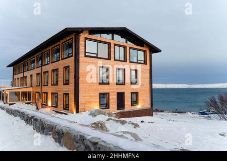 Allein schneebedecktes Haus in den Bergen. Einsames verlassenes rotes Holzhaus am Fuße des schneebedeckten Berges. Winterlandschaft im Norden. Stockfoto