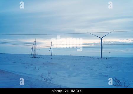 Schneefeld und Windturbine bei Sonnenaufgang im Winter. Luftaufnahme der Natur im Winter. Alternative Energiequellen. Umweltfreundlicher Strom Stockfoto